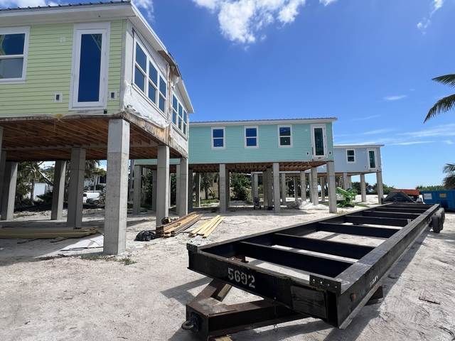Elevated beach houses under construction with concrete pilings and a black trailer in the foreground.