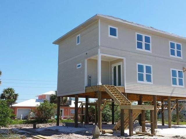 Elevated beige house on stilts with exterior stairs under a clear blue sky.