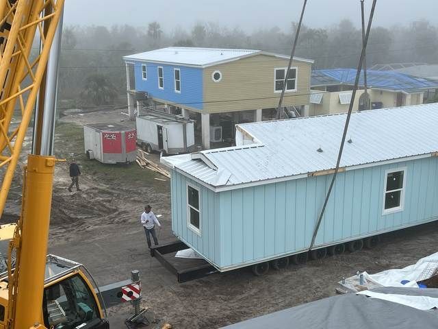 Foggy worksite with two modular buildings and workers near a yellow crane.