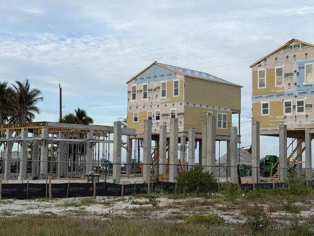 Partially built coastal houses with exposed framing under a cloudy sky.