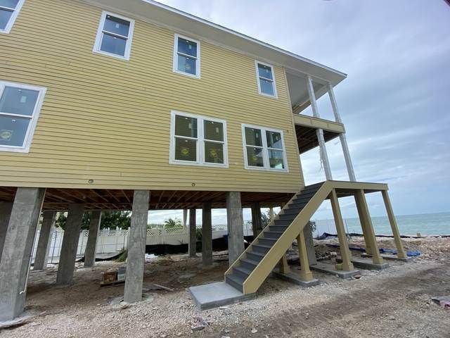 Elevated yellow beach house with stairs on concrete pillars beside the ocean.