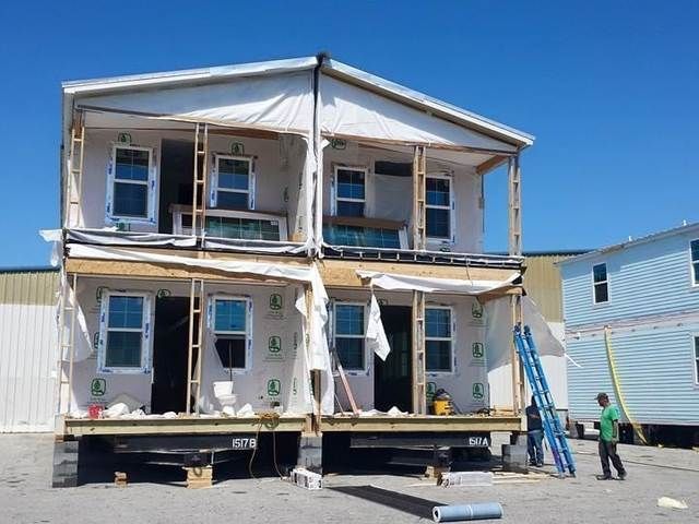 Two-story house under renovation, with exposed framing, blue ladder, and two workers outside.
