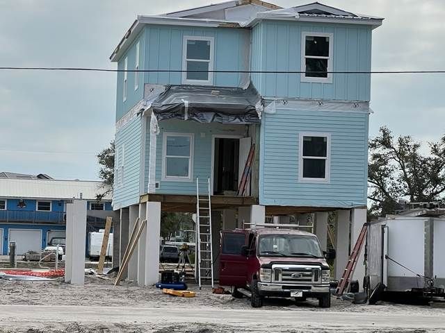 Elevated blue house under construction with exposed stilts and a truck parked below.