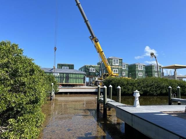 Crane over waterfront construction site beside a canal and modern buildings under a blue sky.