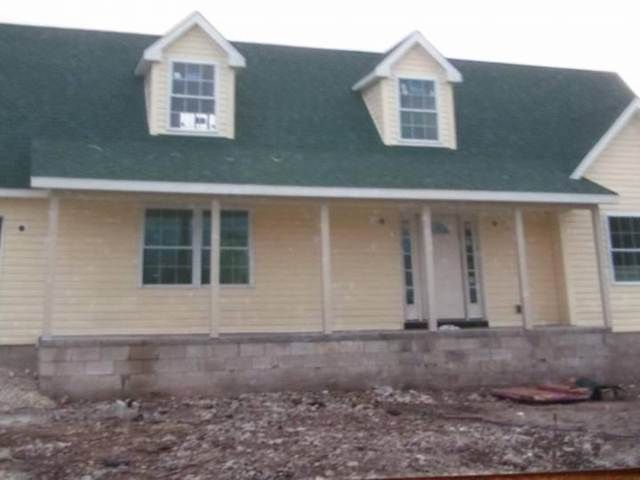 Yellow house with green roof and front porch under construction, with bare ground in front.