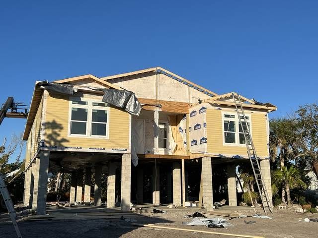 Damaged yellow house under construction, with torn siding and exposed framing after storm damage.