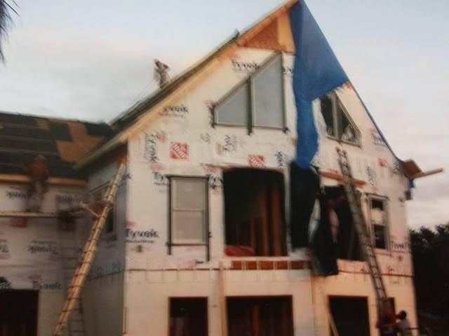Damaged house with exposed roof and broken windows, wrapped in construction scaffolding.