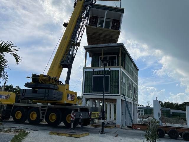 Yellow crane lowering a section onto a white tower under construction outdoors.