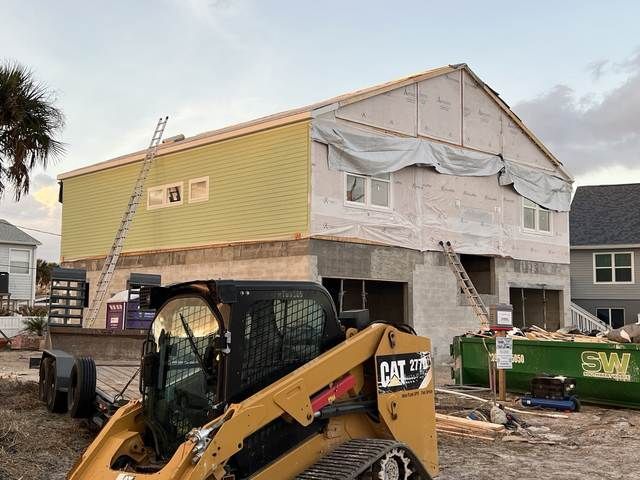 Construction site with a yellow CAT loader in front of a house under renovation.
