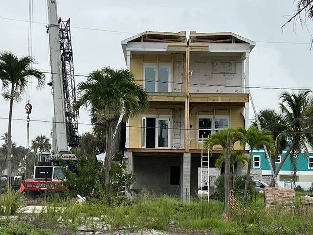 Two-story unfinished house under construction with palm trees and a crane nearby.