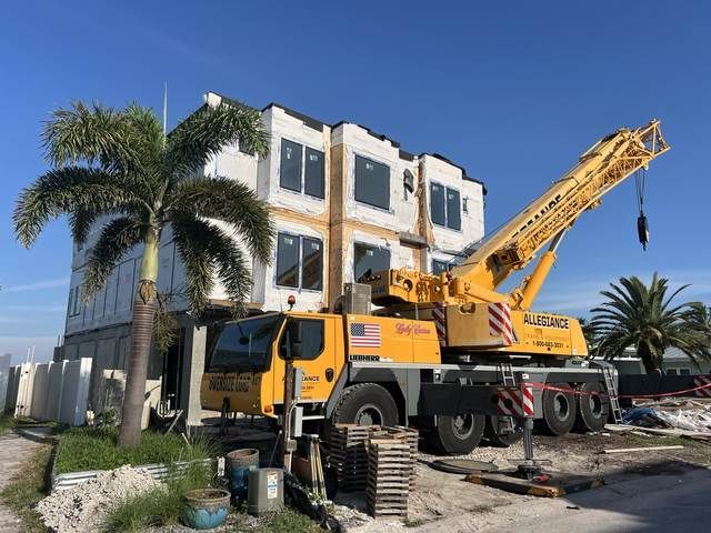 Yellow crane truck parked beside a white building under construction with palm trees and blue sky.