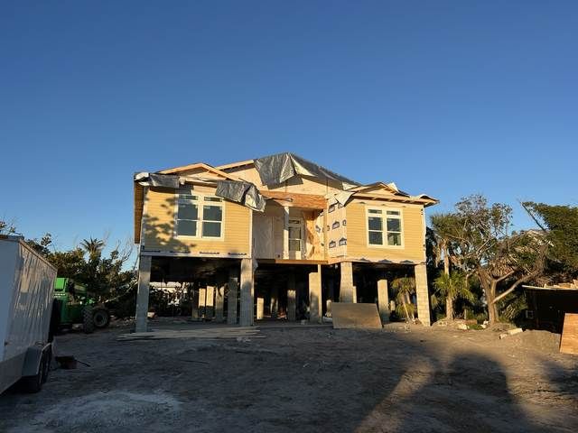 Damaged two-story house under construction with a dirt lot and clear blue sky.