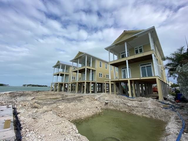 Beachfront houses under construction beside a rocky shoreline and cloudy sky.