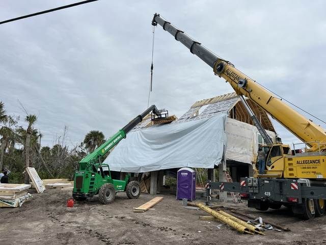 Green and yellow cranes lifting debris from a collapsed house after a storm.