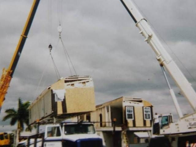 House lifted by cranes onto a truck at a construction site under cloudy skies.