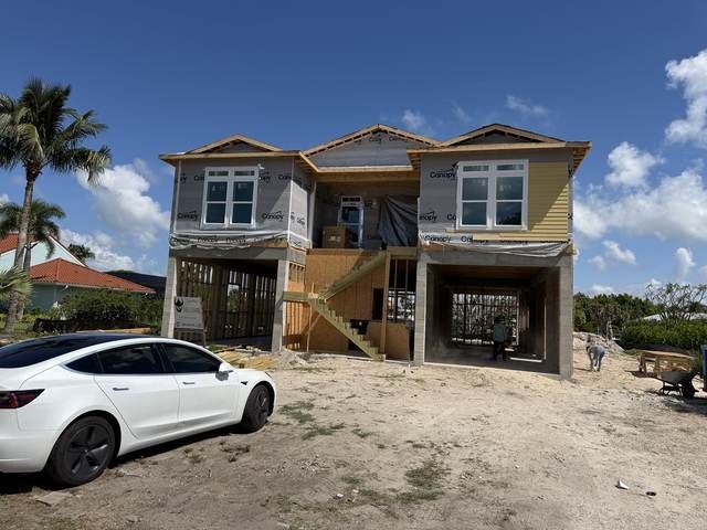 Two-story house under construction with a white car parked in front on a sandy lot.