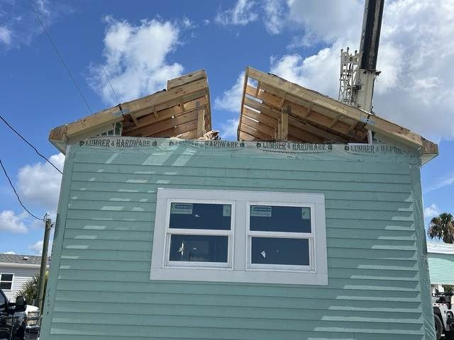 Mint-green house with roof damage and exposed rafters under a blue sky.