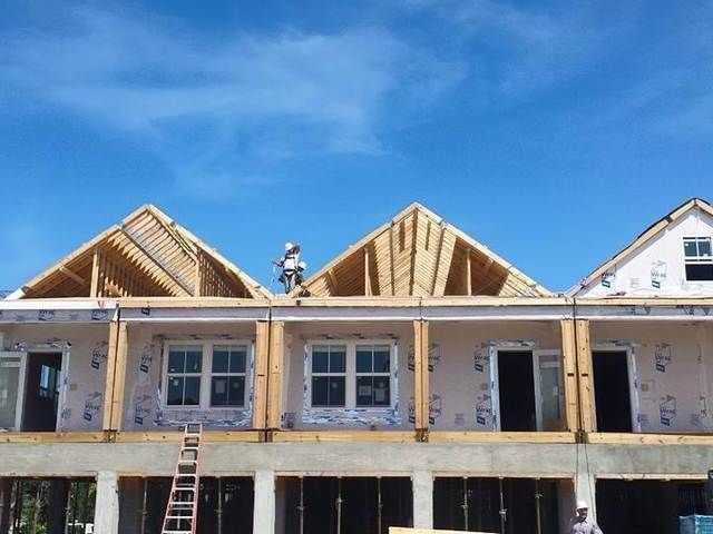 Row houses under construction with exposed roof framing against a blue sky.