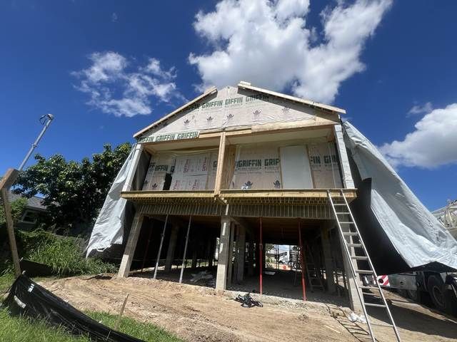 House under construction with scaffolding, tarps, and a ladder beneath a blue sky.