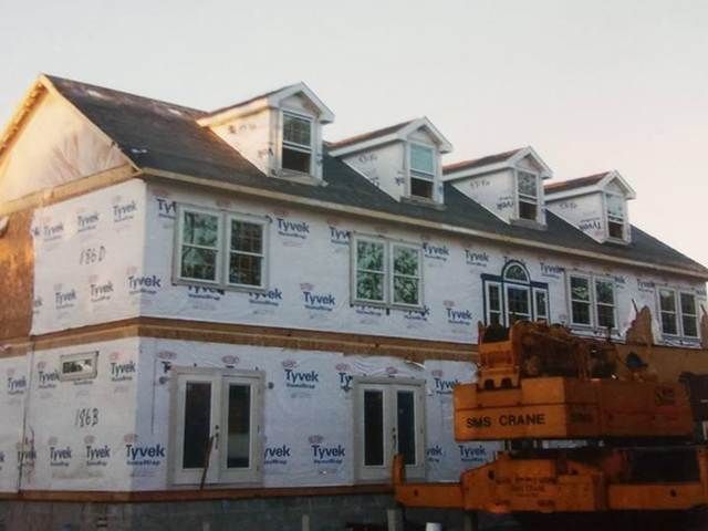 Partially built white two-story house under construction with orange lift in front.