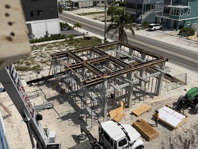Construction site with steel frame of a building, concrete floor, and work trucks nearby.