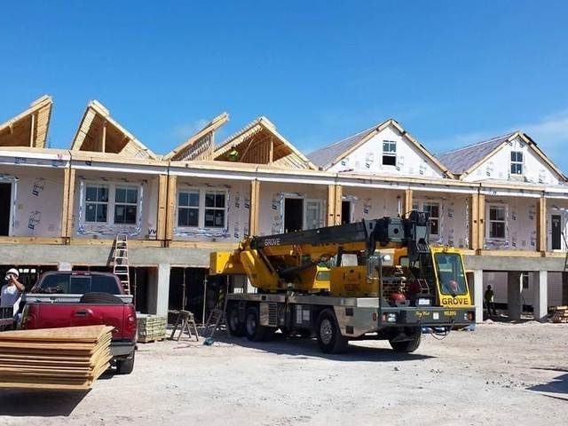 Partially built townhouse row with a crane truck and red pickup in front under a clear blue sky.