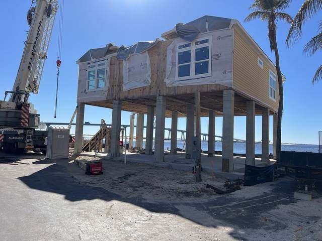 House lifted on stilts by crane on a sunny beach, with palm trees and ocean in the background