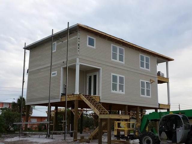 Elevated house under construction on stilts, with stairs, siding, and a tractor below.