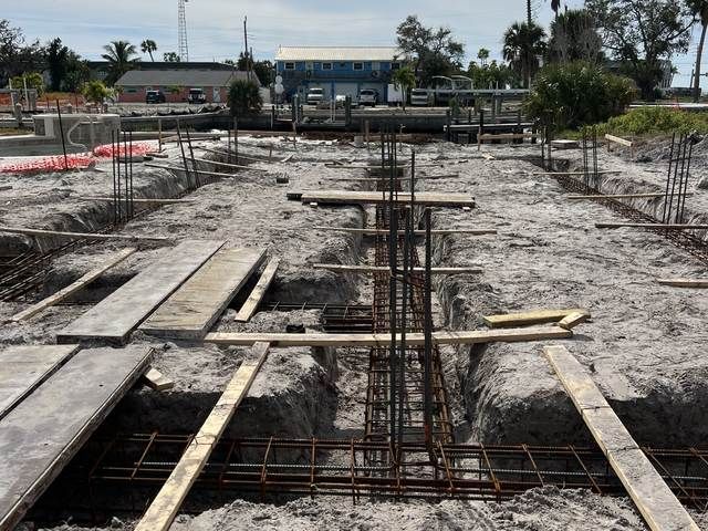 Construction site with reinforced concrete foundation, exposed rebar, and wooden planks on a cleared lot.