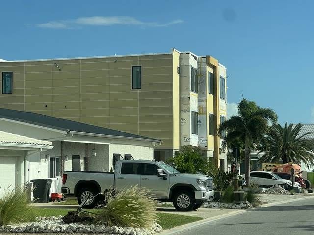 Silver pickup truck parked outside a beige hotel building with palm trees and blue sky.