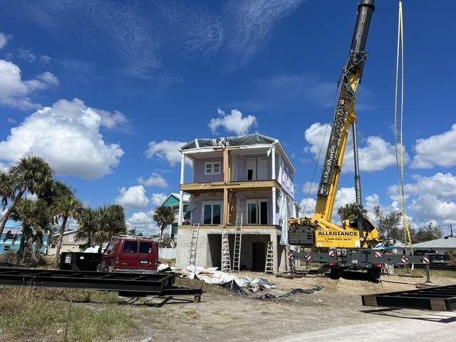 Two-story house under construction with a crane, blue sky, and a red truck nearby.