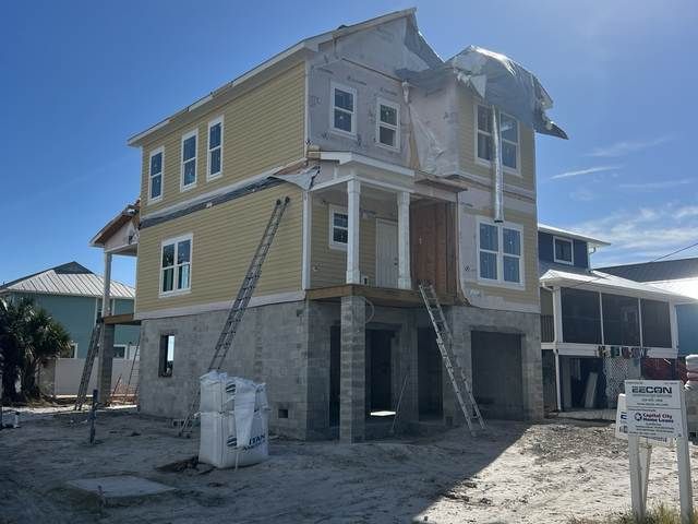 Partially built two-story house with exposed framing and stone base under a bright blue sky.