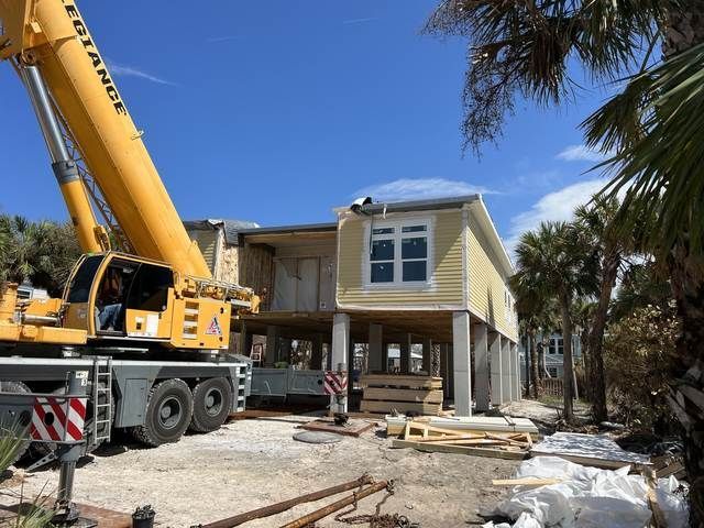 Crane lifting materials at a house under construction beside a yellow two-story home.