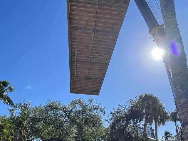 Wooden bridge overhead against blue sky, with palm trees and bright sun below.
