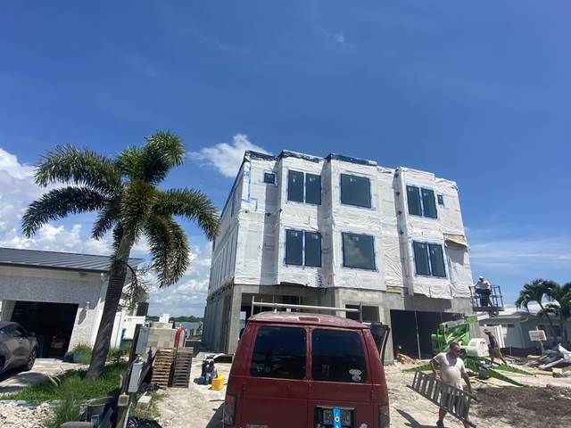 Three-story white building under construction beside a red van and palm tree under a blue sky.
