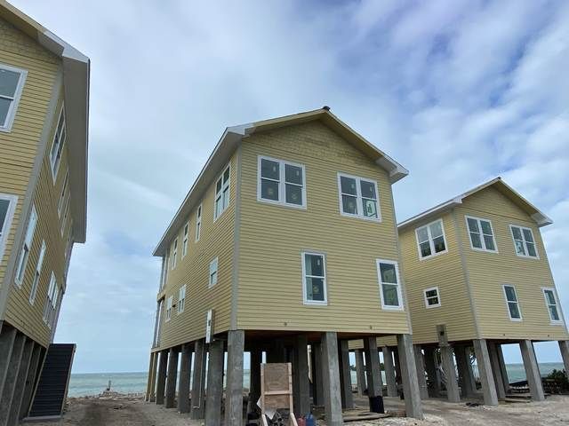 Beach houses on stilts beside the ocean under a cloudy sky.