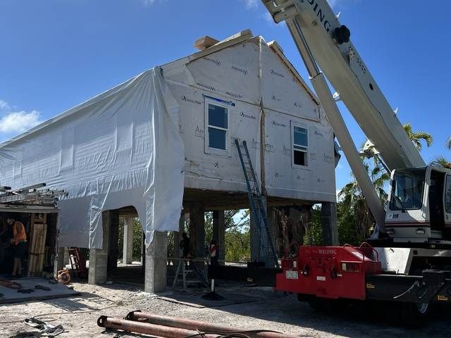 House being lifted by crane during renovation, wrapped in white protective sheeting.