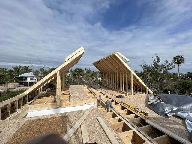 Wood-framed house under construction with two roof sections rising against a cloudy sky.