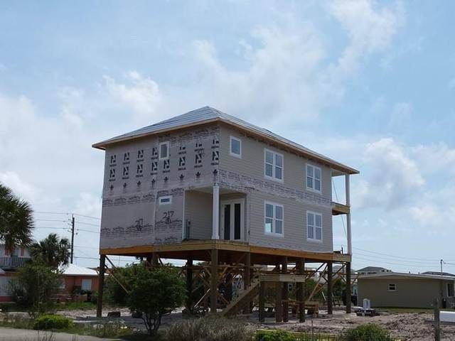 Elevated house under construction on stilts, wrapped in siding with a cloudy sky behind it.