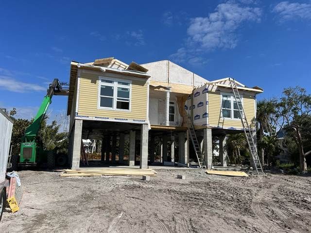 Two-story house under construction with yellow siding, exposed framing, and a green excavator on a dirt lot.