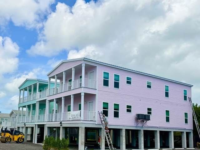 Pastel pink beach house on stilts with balconies, under construction beside a cloudy sky.