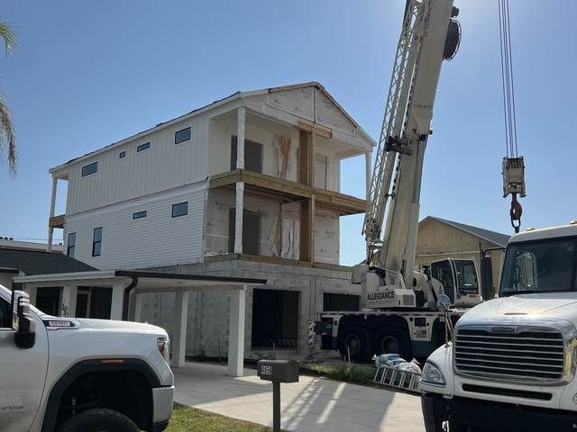 Construction site with a three-story house, crane, and white trucks under a clear blue sky.