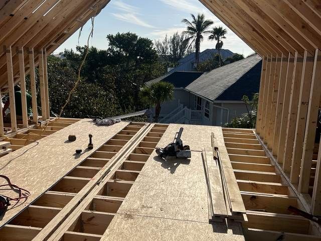 Roof framing under construction with plywood decking and roof trusses, viewed from the attic opening.