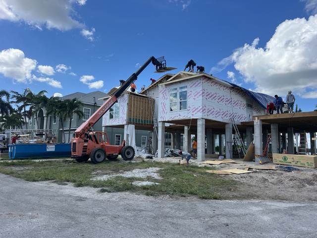 Workers using a crane to install roofing on a house under construction on a sunny day.