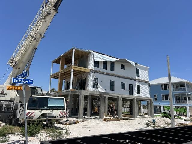 Partially built coastal house with construction crane and workers on a sunny street corner.