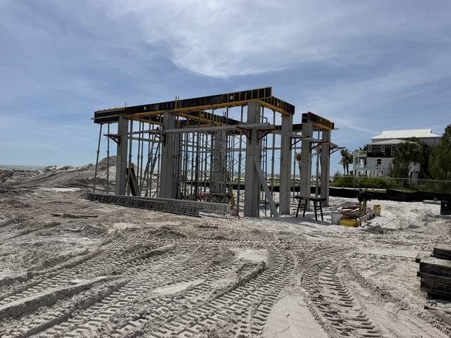 Construction site with a partially built concrete frame on sandy ground under a clear blue sky.