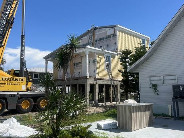 Crane working beside a raised house under construction on a sunny day.