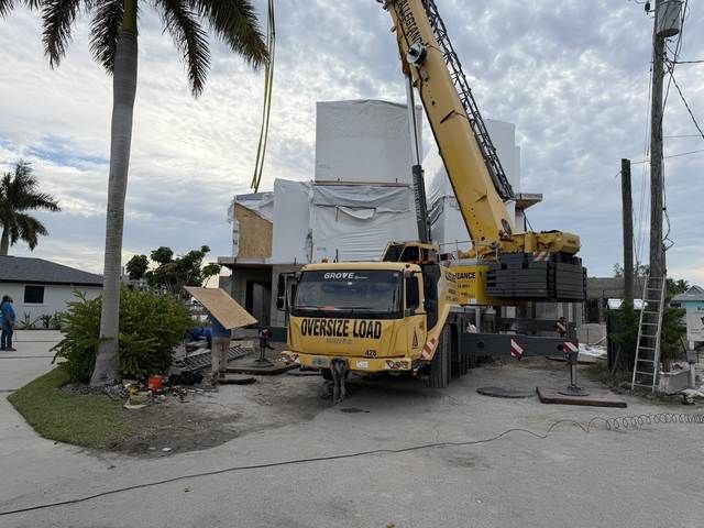 Yellow crane truck lifting debris beside a white building on a street with palm trees.