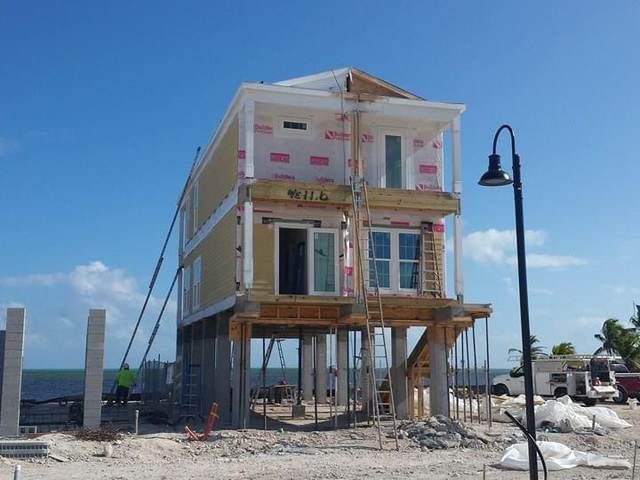 Partially built seaside house on stilts with exposed framing under a blue sky.