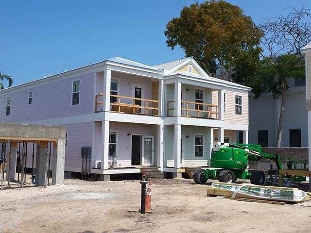 Two-story white house under construction with a green lift and building materials in front.